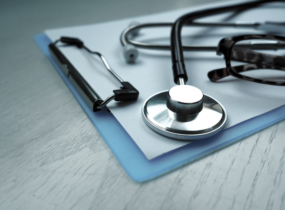 Close-up of a stethoscope on a clipboard with medical documents and glasses on a desk, symbolizing healthcare and medical professionalism.